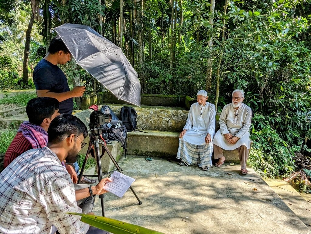 চাঁদপুরের গ্রামীণ লোকেশনে প্রখর রোদ থেকে ক্যামেরা আড়াল করে প্রবীণ নৌ-কমান্ডো ও মুক্তিযোদ্ধাদের সাক্ষাৎকার গ্রহণ